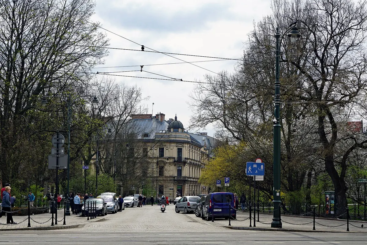 Sławkowska Street seen from its northern end, a cobbled street lined with trees and parked cars, with a corner building under a small dome at its far end.